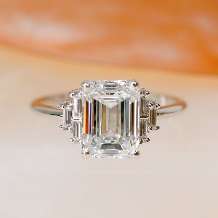 an emerald - cut diamond ring with baguettes sits on a table