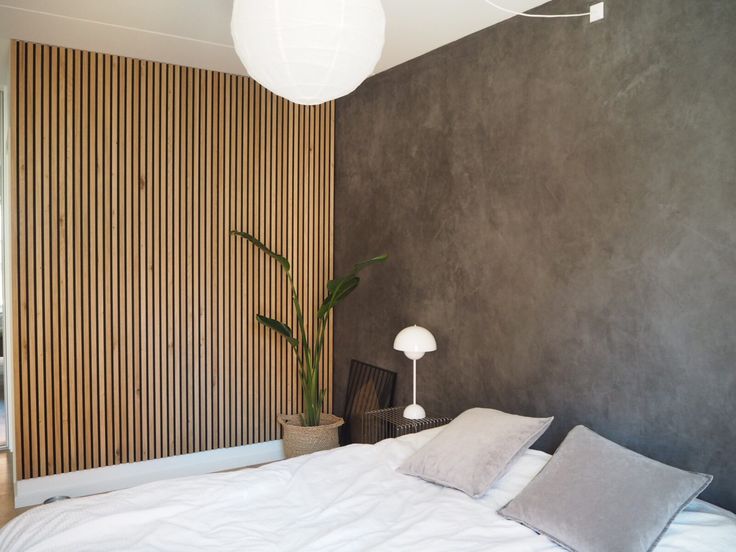 a bed with white sheets and pillows in a bedroom next to a wall mounted lamp