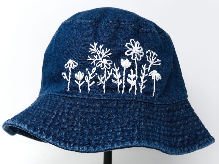 a blue hat with white flowers embroidered on the front and side, sitting on a wooden stand