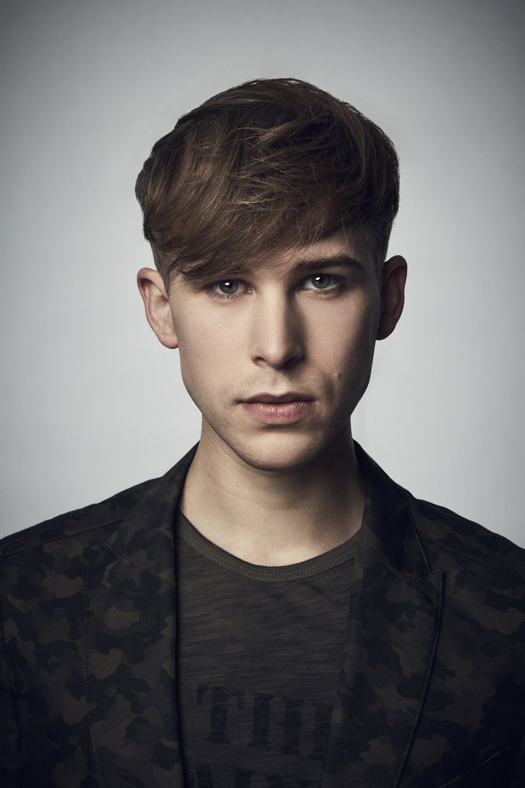 a young man is posing for the camera in front of a gray background and wearing a black jacket