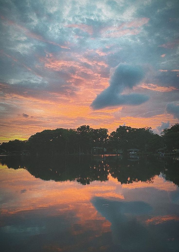 the sky is reflecting in the water at sunset or sunrise, as seen from across the lake