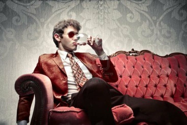 a man sitting on top of a red couch drinking from a cup in his hand