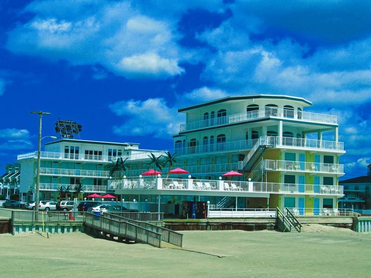 an ocean side hotel with cars parked on the beach and umbrellas in front of it