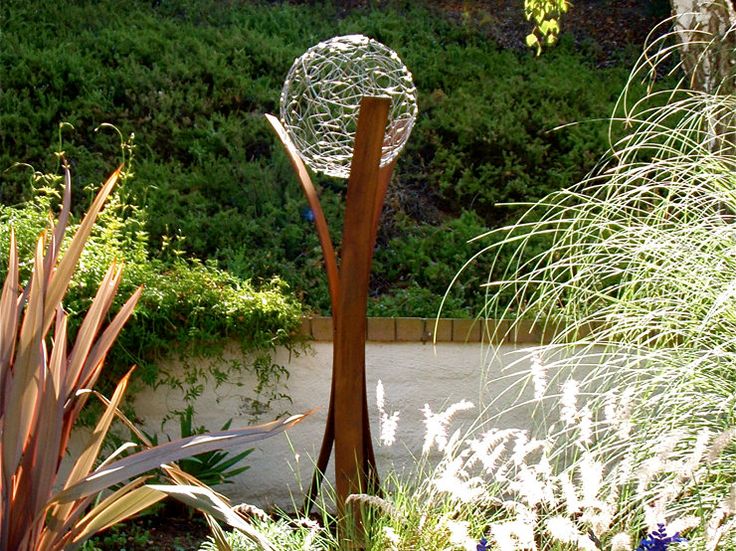 an outdoor garden with plants, flowers and a sculpture in the foreground on a sunny day