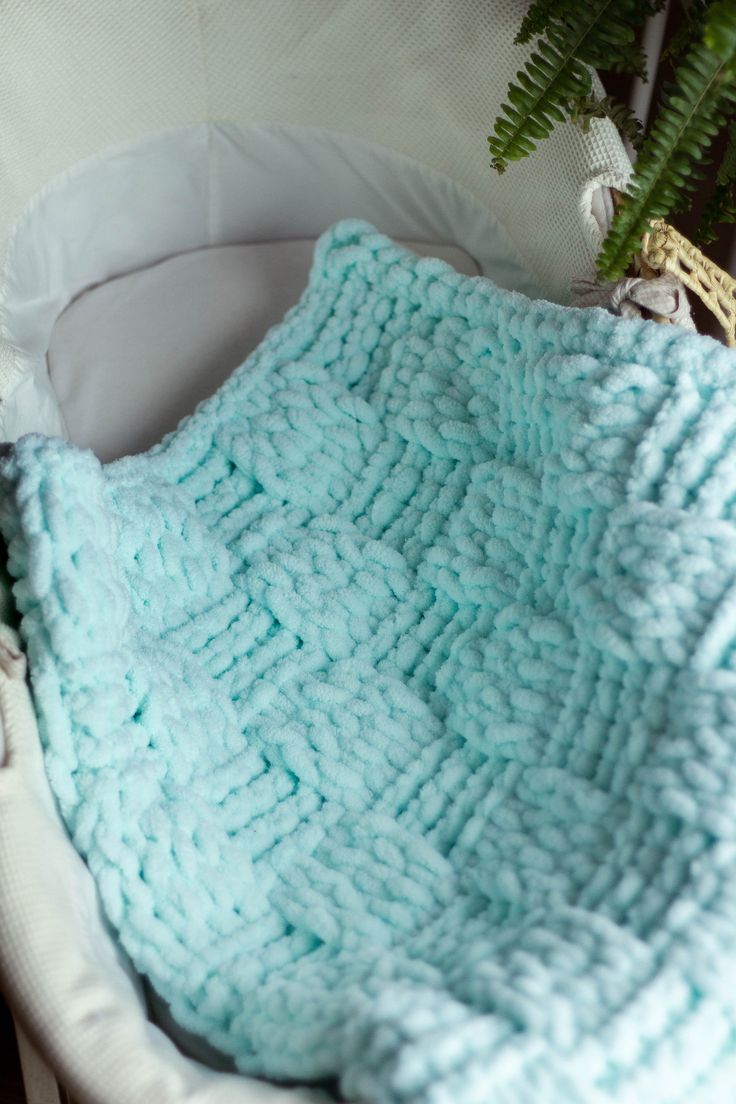 a crocheted blanket sitting in a basket next to a potted plant