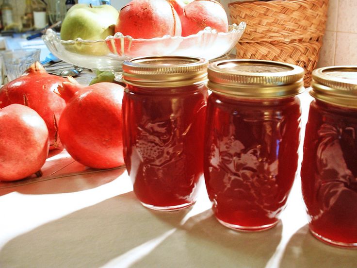 four jars filled with red liquid sitting on top of a table next to apples and pears