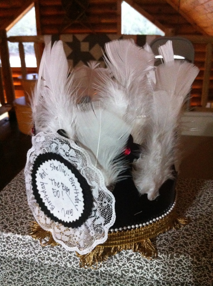 a black hat with white feathers and a clock on the top is sitting on a table