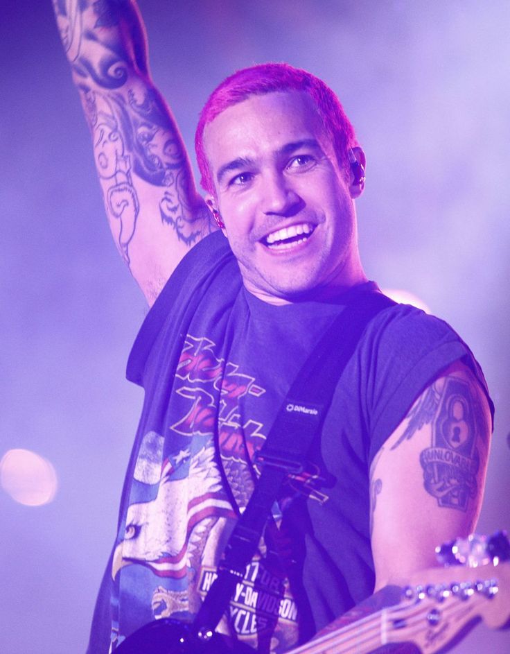 a man with tattoos on his arm holding a guitar in front of him and smiling at the camera