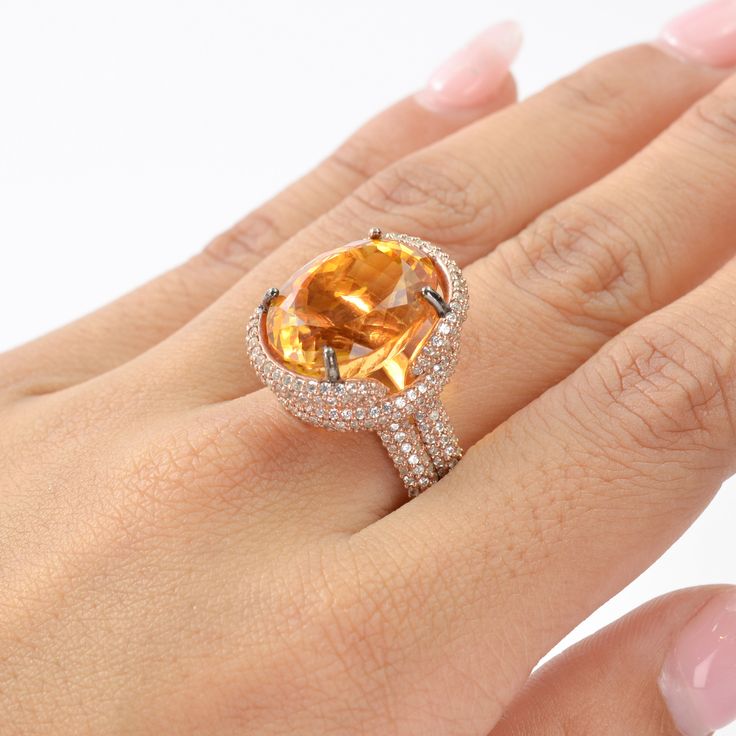 This exquisite ring features a stunning Citrine as the center stone, radiating vibrant hues of golden yellow. The Citrine is complemented by an array of White Zircon accent stones, adding a touch of brilliance and sparkle to the piece. The design showcases a luxurious rose gold-plated band, enhancing the warm tones of the Citrine. The intricate setting highlights the gemstone's natural beauty, making it a perfect statement piece for any occasion. This piece is inspired by the Art Deco era, known Dazzling Oval Yellow Ring, Dazzling Yellow Oval Ring, Luxury Gold Rings With Gemstone Accents, Gold Topaz Crystal Ring With Gemstone, Yellow Open Ring Fine Jewelry, Luxury Orange Gemstone Ring, Luxury Citrine Rings For Anniversary, Yellow Diamond Gemstone Ring Fine Jewelry, Elegant Citrine Crystal Ring