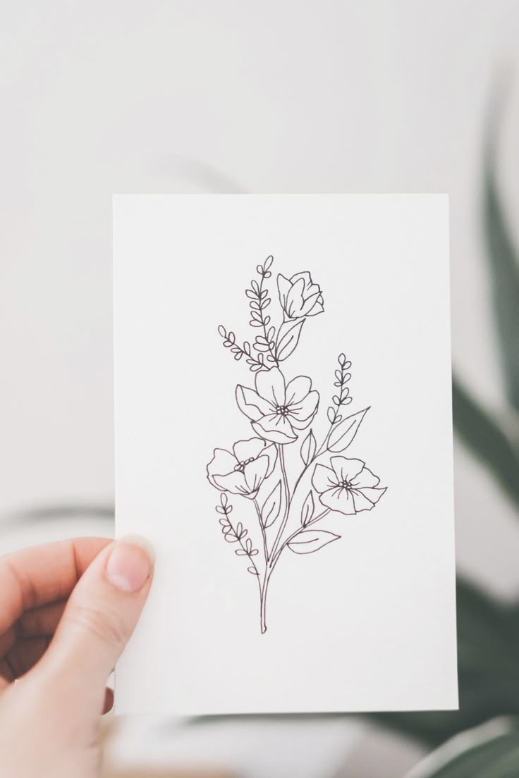 a person holding up a card with some flowers on it and a plant in the background