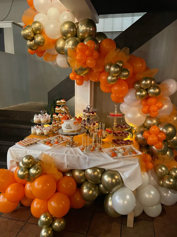 an orange and white dessert table with balloons