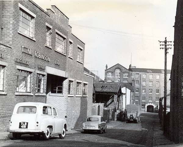 an old black and white photo of cars parked on the side of a road in front of brick buildings