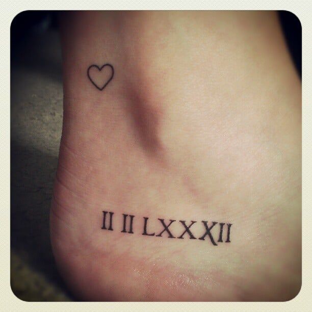 a small foot tattoo with roman numerals and a heart on the top one