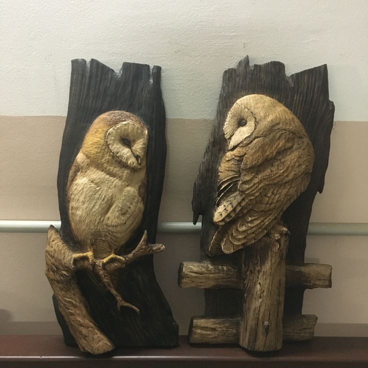 two carved wood owls sitting on top of wooden logs in front of a white wall