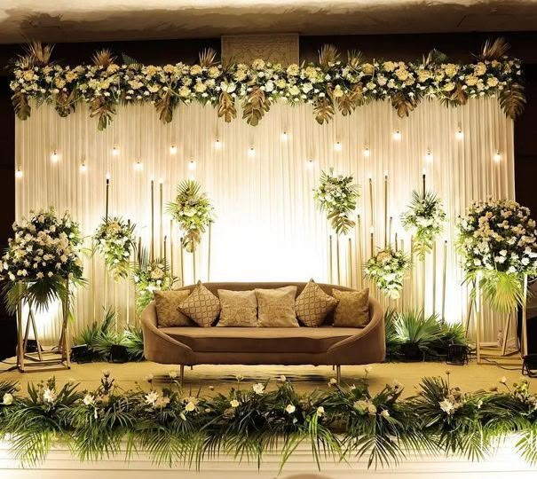 a couch sitting in front of a stage with flowers and greenery on the wall