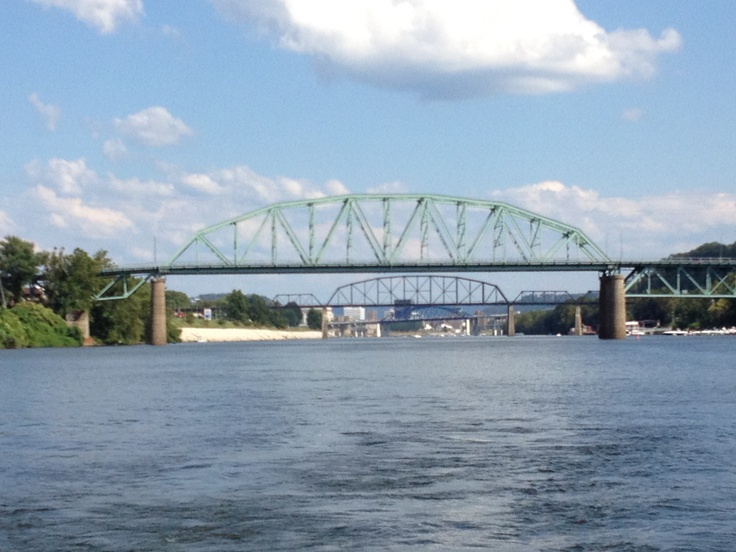 a green bridge spanning the width of a body of water under a cloudy blue sky