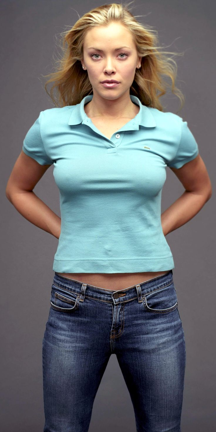 a woman with her hands on her hips standing in front of a gray background and looking at the camera