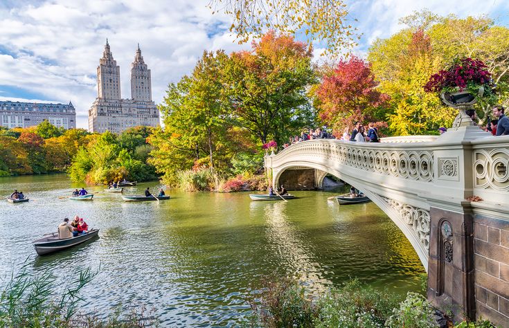 people are riding boats on the river in central park, with fall foliage around them