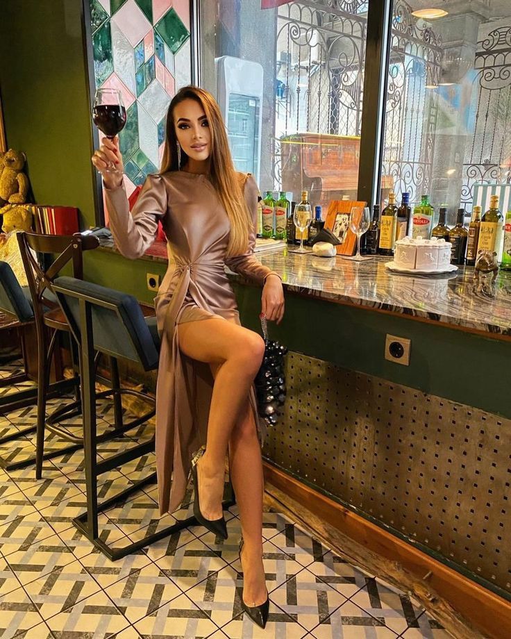 a woman sitting at a bar holding a wine glass in one hand and looking into the camera