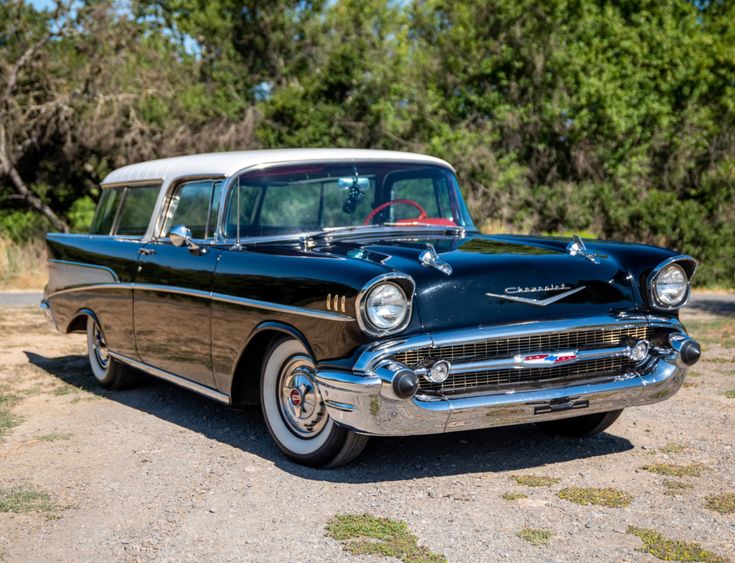 an old black and white car is parked in the dirt