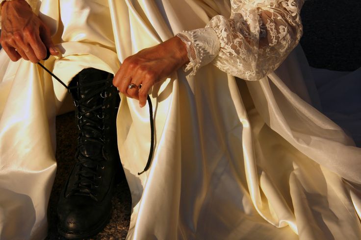 a woman in white dress sitting on the ground tying up her lace covered booties