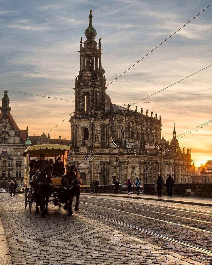 horse drawn carriage on cobblestone road in front of large building with spires