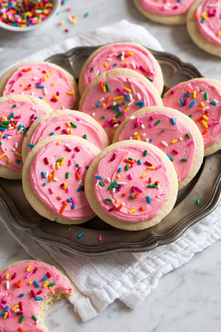 cookies with pink frosting and sprinkles on a silver platter next to bowls of sprinkles