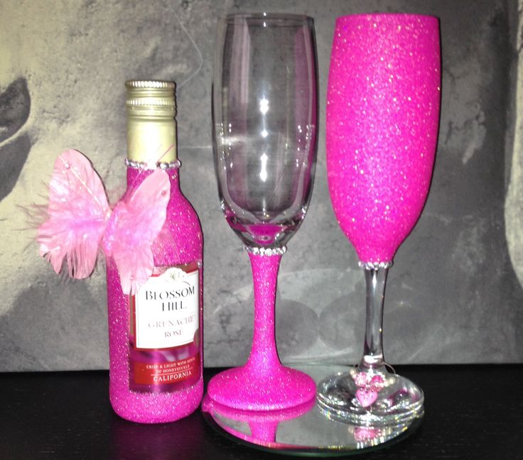 two wine glasses, one pink and the other red with a bow on it next to a bottle of booze