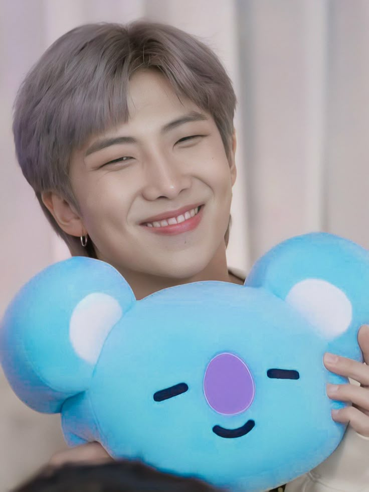 a man holding a blue teddy bear pillow in front of his face and smiling at the camera