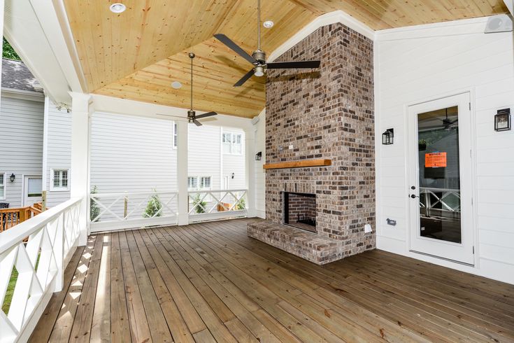 a porch with a ceiling fan and brick fireplace on the front deck area, surrounded by white shutters