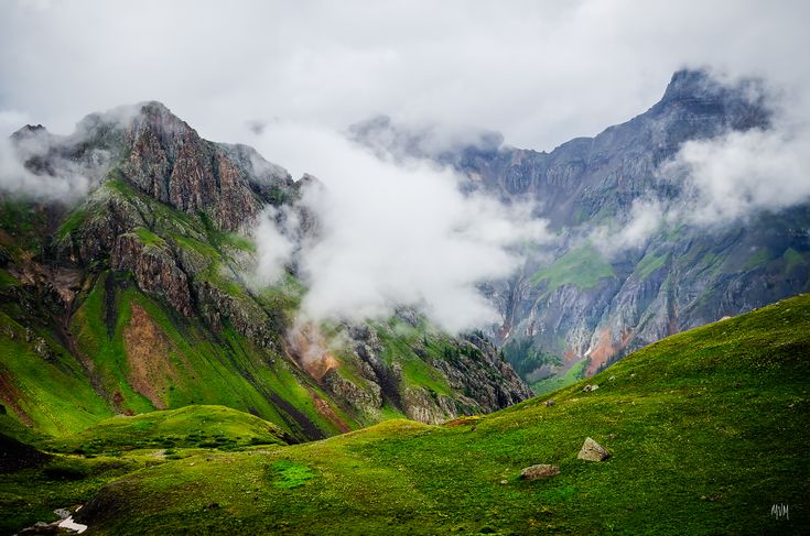 the mountains are covered in clouds and green grass