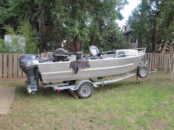 a boat parked on the grass in front of a fenced area with a motorboat attached to it