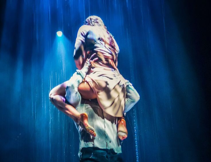 a man holding onto another mans back in the rain at a music festival or concert