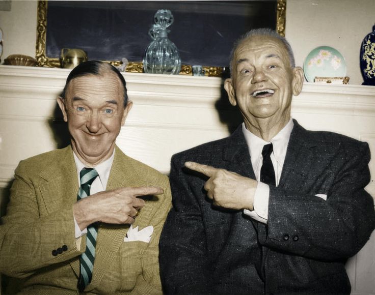 two men in suits sitting next to each other pointing at something with their fingers and smiling