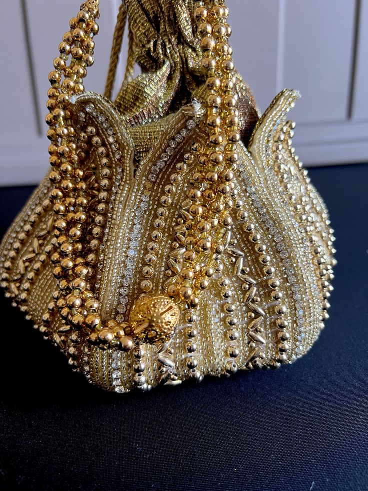 Looking for a stylish and trendy accessory to complete your ethnic ensemble? Look no further than our stunning Gold color potli bag! Handcrafted with care and attention to detail, this elegant bag is the perfect way to add some extra sparkle to your special occasion outfit. Made from high-quality materials, this potli bag features a shimmering gold color that catches the light beautifully. The soft, luxurious texture of the fabric is complemented by intricate embroidery and beadwork, creating a Bollywood Style Shoulder Bag With Zari Work, Handwork Shoulder Bag For Diwali, Festive Beaded Evening Bag For Reception, Elegant Festival Bags For Festive Occasions, Elegant Festive Bags For Festival, Elegant Festival Bags, Elegant Festive Potli Bag With Dori Work, Elegant Beaded Festive Bags, Beaded Potli Bag For Party