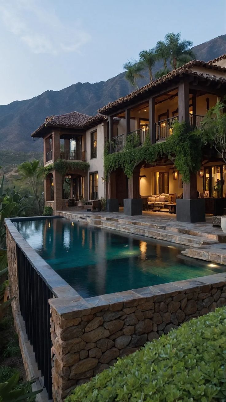 an outdoor swimming pool in front of a large house with mountains in the back ground