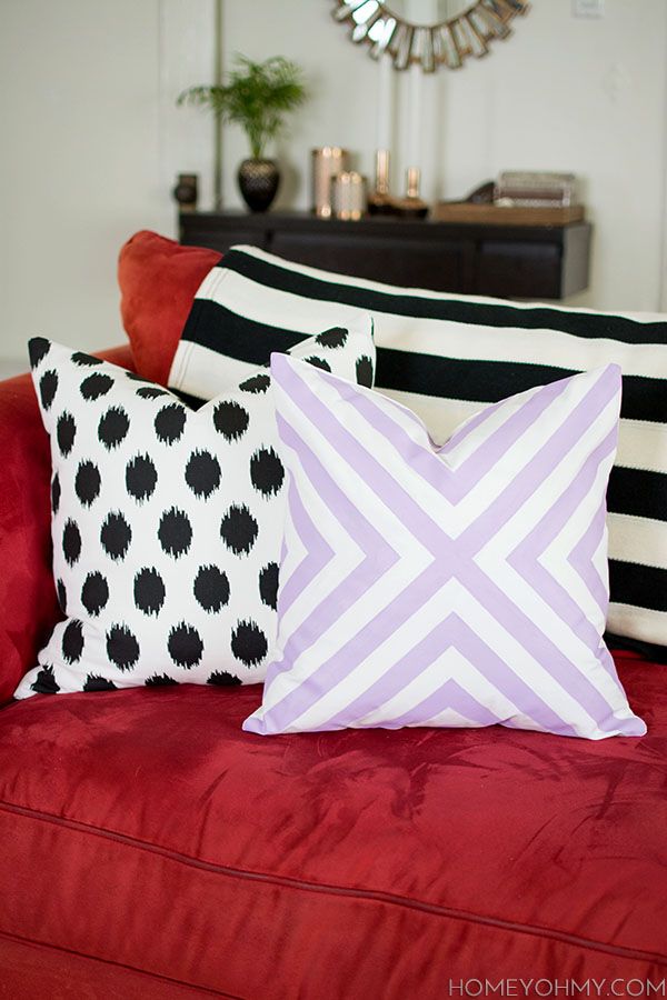 three pillows sitting on top of a red couch next to a mirror and vases