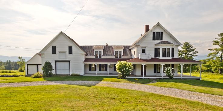 a large white house sitting in the middle of a lush green field next to a road