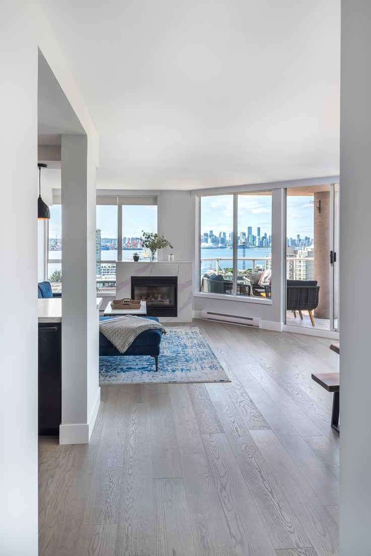 an empty living room with wood floors and large windows overlooking the cityscape in the distance