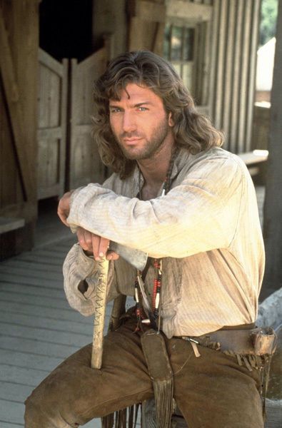 a man with long hair and beard holding a stick in his hand while sitting on a porch