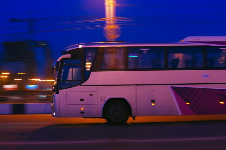 a white bus driving down the road at night with traffic lights in the back ground