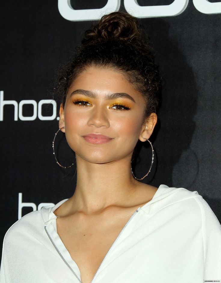 a woman with large hoop earrings on her head and white shirt in front of a black background