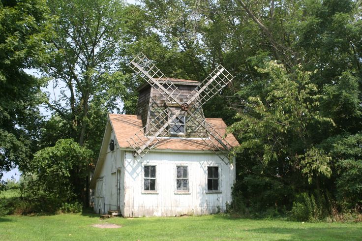 an old white house with a windmill on the roof and some trees in the background