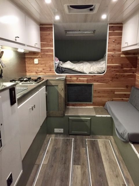 the interior of a camper with wood flooring and white cabinets, including a bed