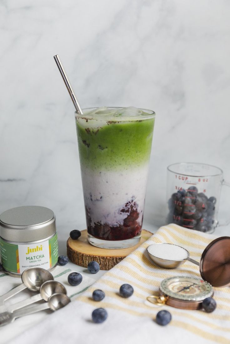 a green drink with blueberries and yogurt on the side next to measuring spoons