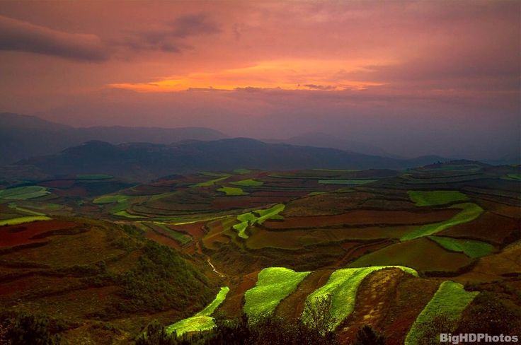 the sun is setting over rolling hills and fields with green grass in the foreground