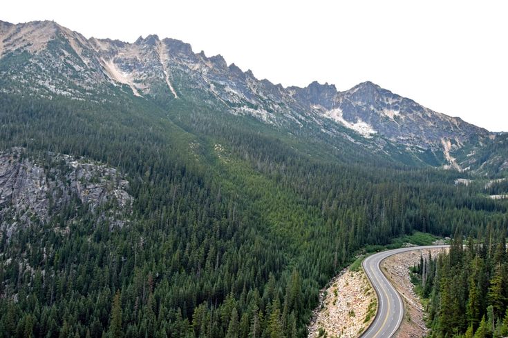 an aerial view of a winding road in the mountains with pine trees and evergreens