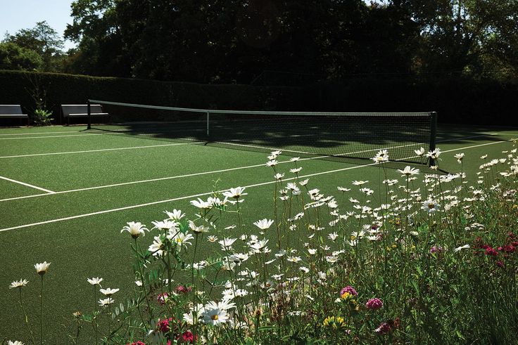 two tennis courts surrounded by wildflowers on a sunny day with trees in the background