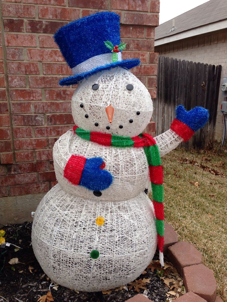 a snowman made out of wire sitting in front of a brick wall