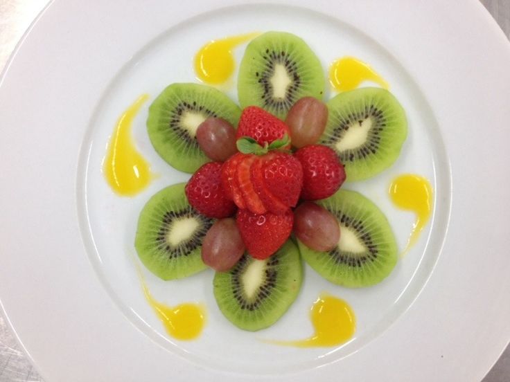 a white plate topped with sliced kiwis and strawberries on top of syrup